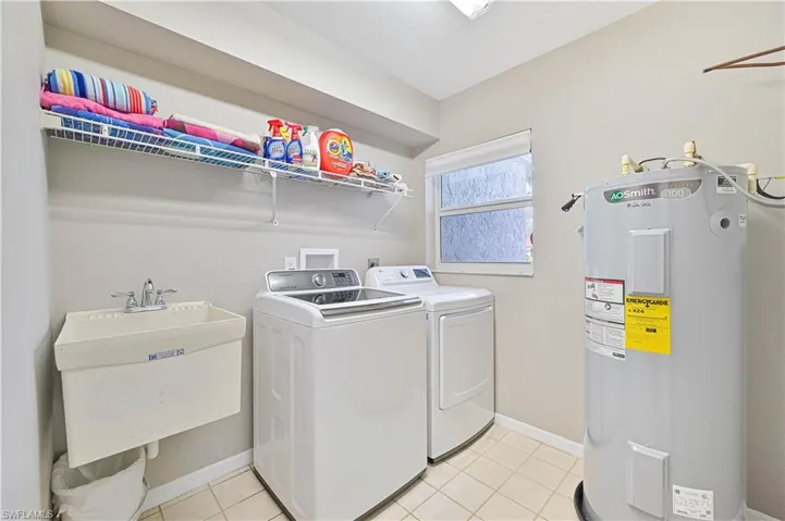 Laundry area featuring washer and dryer, light tile patterned floors, electric water heater, and sink