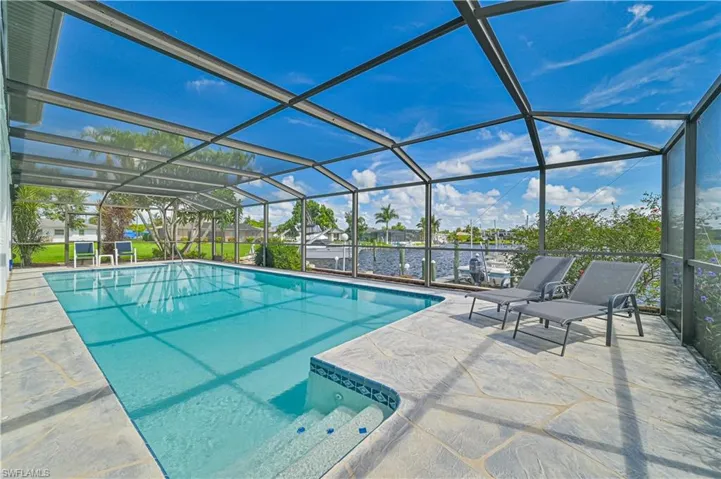 View of swimming pool with glass enclosure, a patio, and a water view