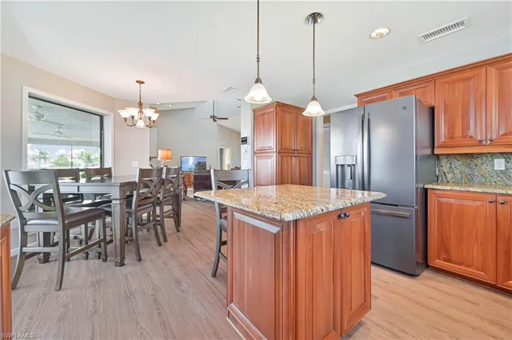 Kitchen with a kitchen island, ceiling fan with notable chandelier, stainless steel fridge, backsplash, and light hardwood / wood-style floors