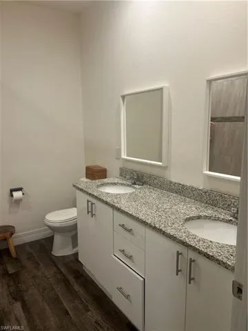 Bathroom featuring a dual vanity with white cabinetry, speckled granite countertop, and integrated sinks