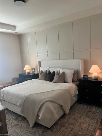 Bedroom featuring board and batten accent wall, recessed ceiling detail, and patterned area rug on wood-finish flooring