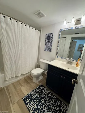 Bathroom featuring vanity, toilet, visible vents, shower / bath combination with curtain, and wood finished floors