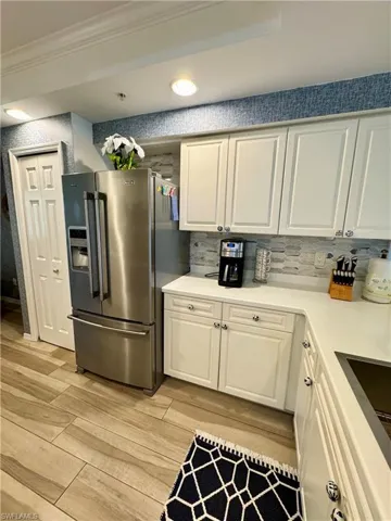 Kitchen featuring light countertops, stainless steel fridge with ice dispenser, white cabinetry, wood finish floors, and ornamental molding