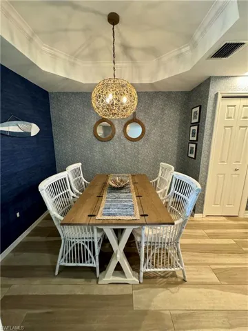 Unfurnished dining area with visible vents, crown molding, wallpapered walls, light wood-type flooring, and a notable chandelier