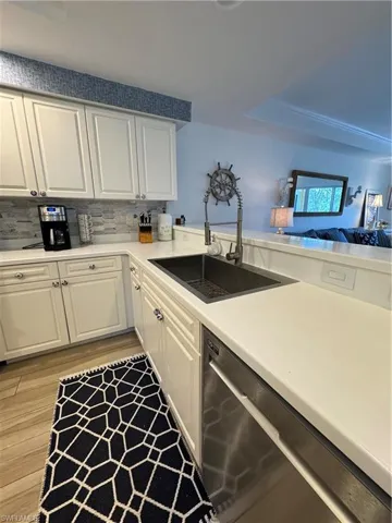 Kitchen with white cabinetry, tasteful backsplash, a sink, light wood-style floors, and dishwasher