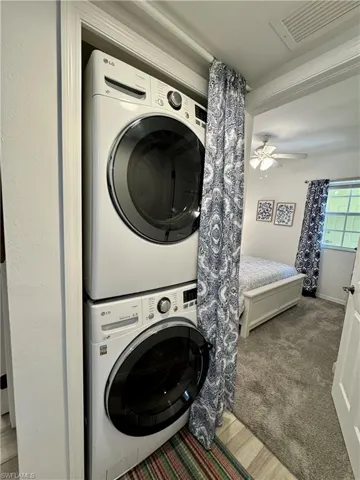 Laundry room featuring carpet flooring, stacked washing maching and dryer, laundry area, visible vents, and ceiling fan