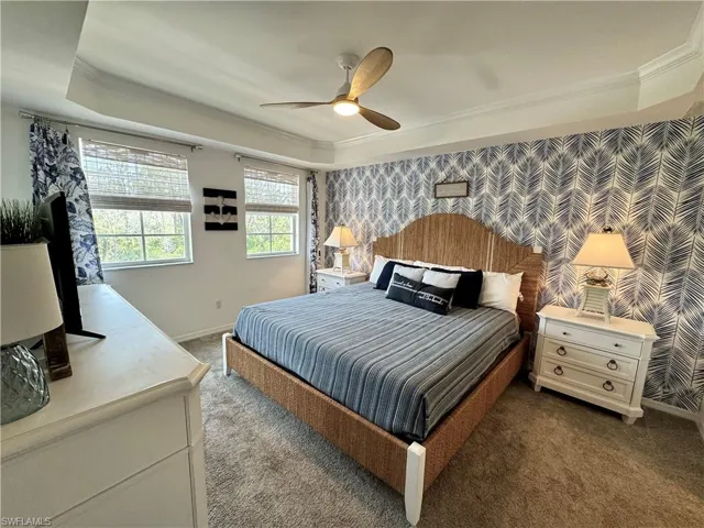 Carpeted bedroom with crown molding, baseboards, wallpapered walls, a raised ceiling, and ceiling fan