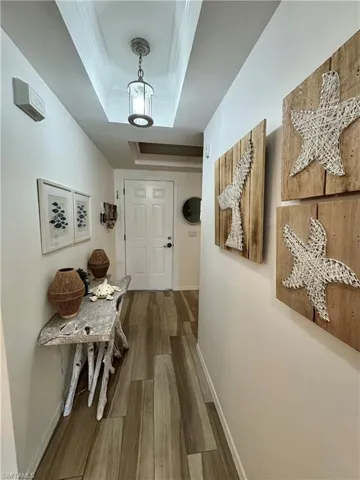 Hall featuring a tray ceiling, baseboards, wood finished floors, and ornamental molding (some items removed)
