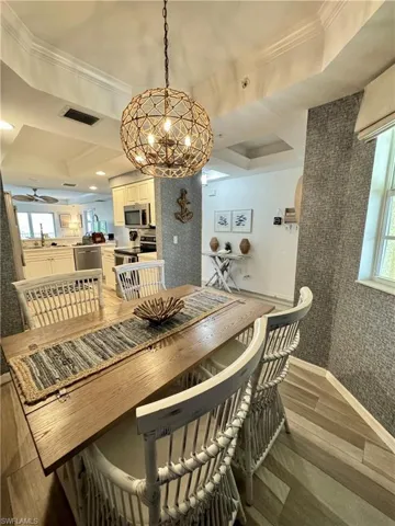 Dining area with wallpapered walls, ceiling fan with notable chandelier, visible vents, light wood-style floors, and ornamental molding
