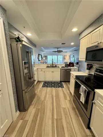 Kitchen with a sink, a raised ceiling, appliances with stainless steel finishes, a peninsula, and wood tiled floor