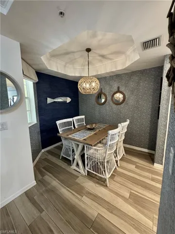 Dining room featuring wallpapered walls, wood finished floors, a tray ceiling, and visible vents