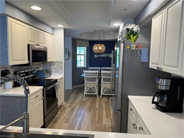 Kitchen with crown molding, light countertops, a raised ceiling, appliances with stainless steel finishes, and light wood-type flooring