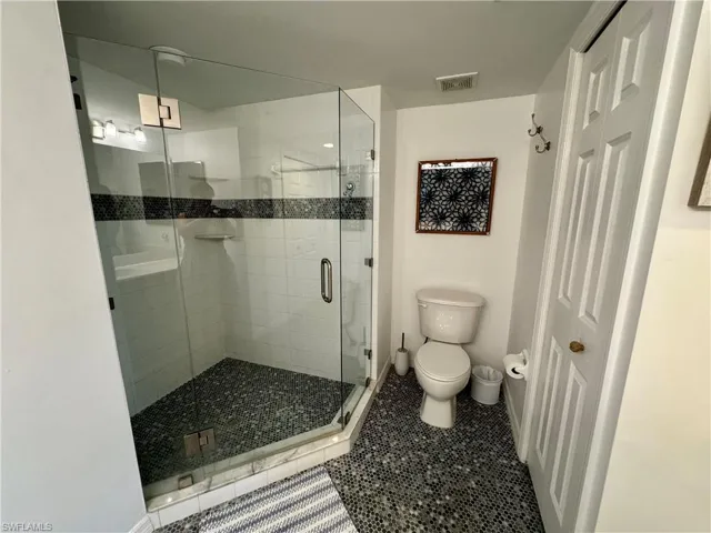 Full bathroom with toilet, a stall shower, tile patterned flooring, and visible vents