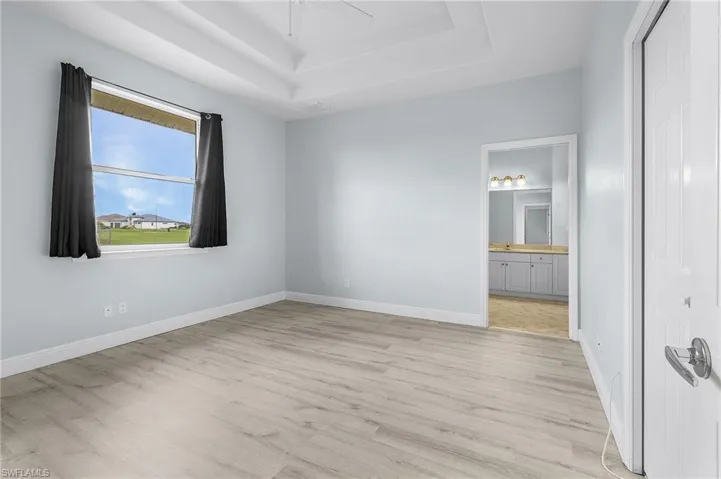 Second master bedroom featuring a double tray ceiling, connected bathroom, ceiling fan, and light vinyl plank flooring.