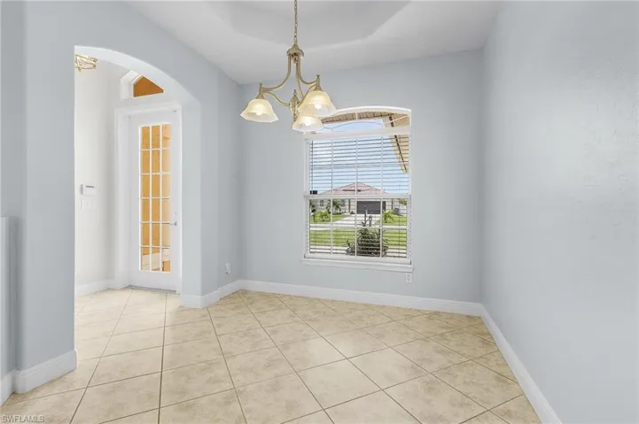 Formal dining room with double tray ceiling, light tile patterned flooring, and a notable chandelier