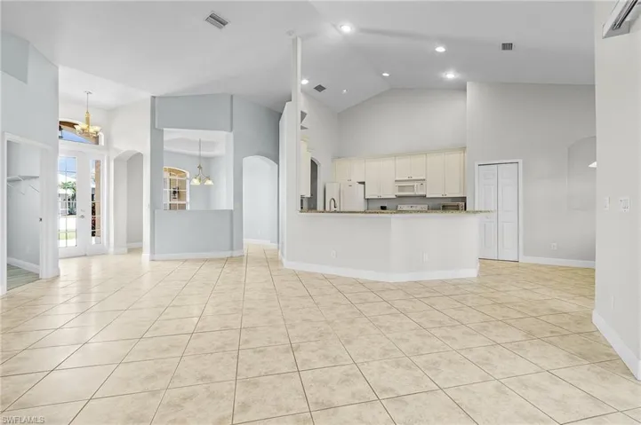Kitchen with decorative light fixtures, white appliances, light stone counters, a chandelier, and high cathderal ceiling.