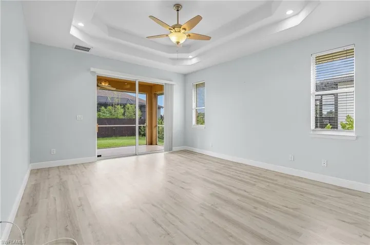Master bedroom featuring a double tray ceiling, light vinyl plank flooring, sliders to lanai and ceiling fan.