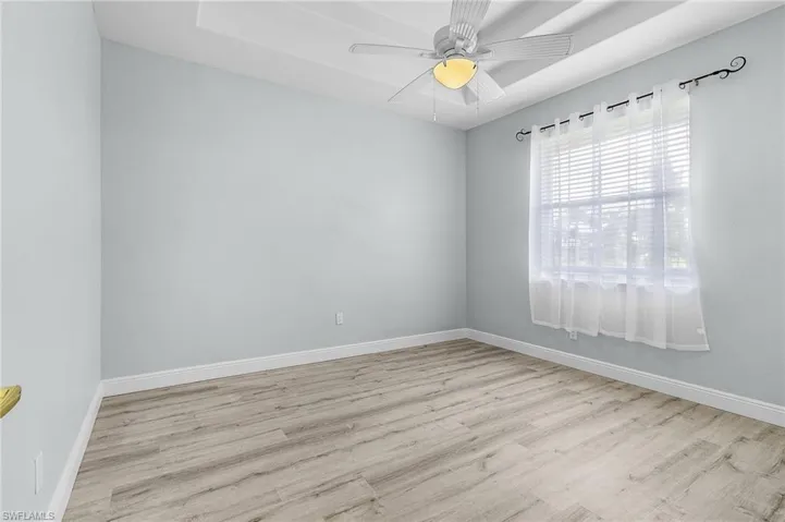 Guest bedroom with light vinyl plank flooring, double tray ceiling and ceiling fan.