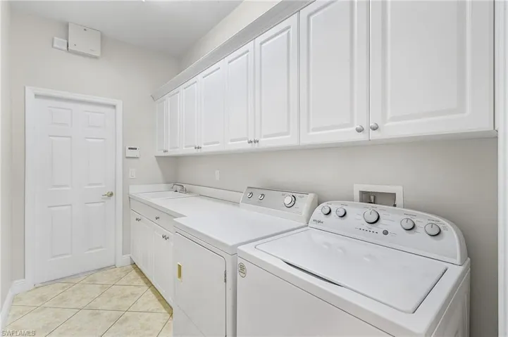 Laundry room with light tile patterned floors, cabinets, washer, dryer, cabinets and laundry tub.