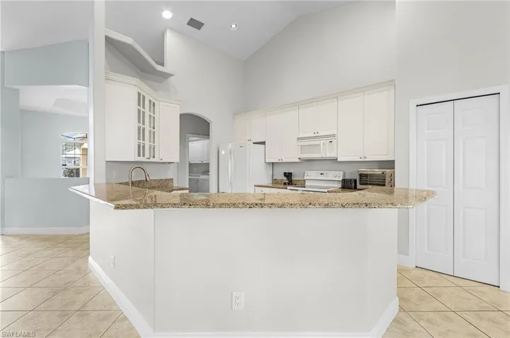 Island kitchen with granite tops, breakfast bar, newer white appliances, and light tile patterned flooring.