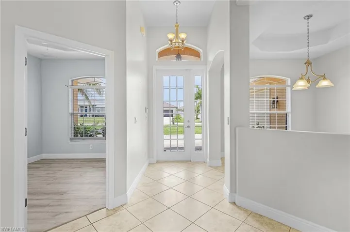 Entryway with a tray ceiling, light tile patterned floors, and a notable chandelier