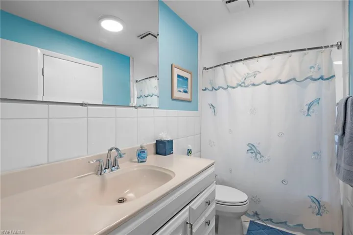 Bathroom featuring a shower with curtain, vanity, toilet, and tile walls