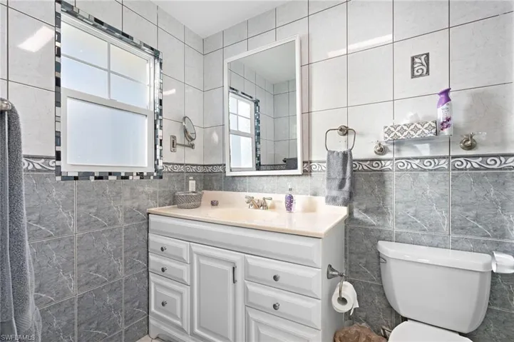 Bathroom featuring vanity, toilet, and tile walls