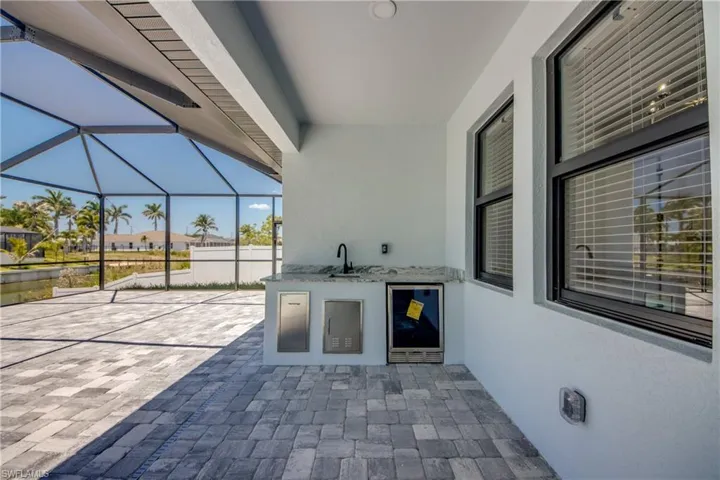 View of patio with glass enclosure, a sink, area for grilling, and wine cooler
