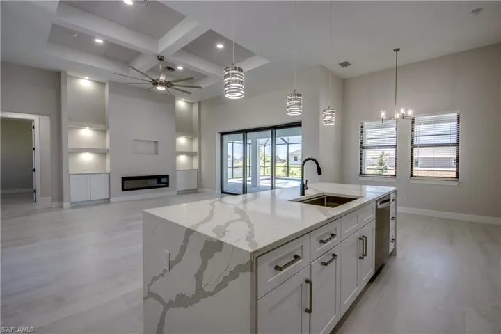 Kitchen with stainless steel dishwasher, baseboards, a sink, coffered ceiling, and ceiling fan with notable chandelier