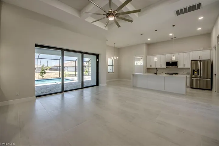 Unfurnished living room featuring a healthy amount of sunlight, a towering ceiling, ceiling fan with notable chandelier, and visible vents