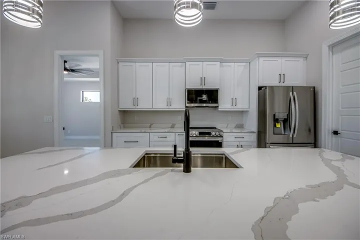 Kitchen featuring hanging light fixtures, white cabinets, stainless steel appliances, and a sink