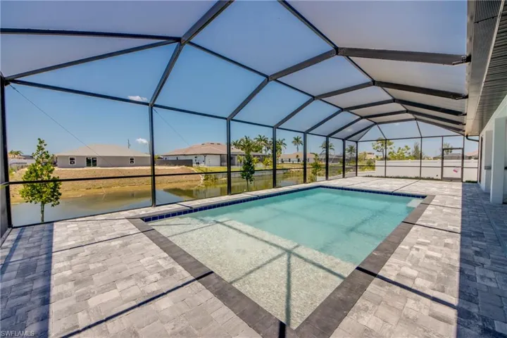 Outdoor pool featuring a residential view, glass enclosure, a water view, and a patio area