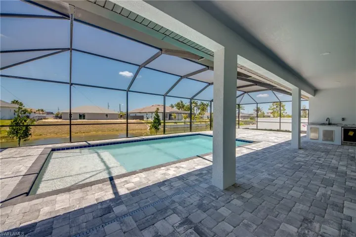 Pool featuring an outdoor kitchen, a patio, glass enclosure, and a residential view