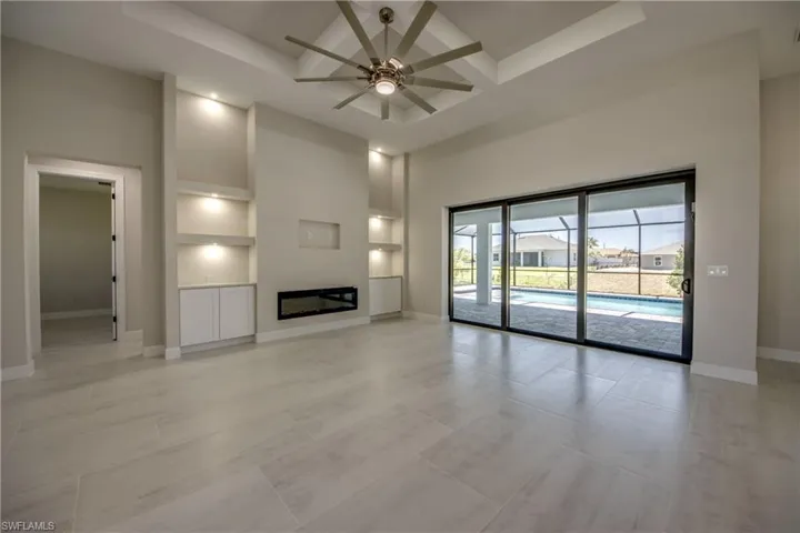 Unfurnished living room with built in shelves, a ceiling fan, baseboards, a towering ceiling, and coffered ceiling