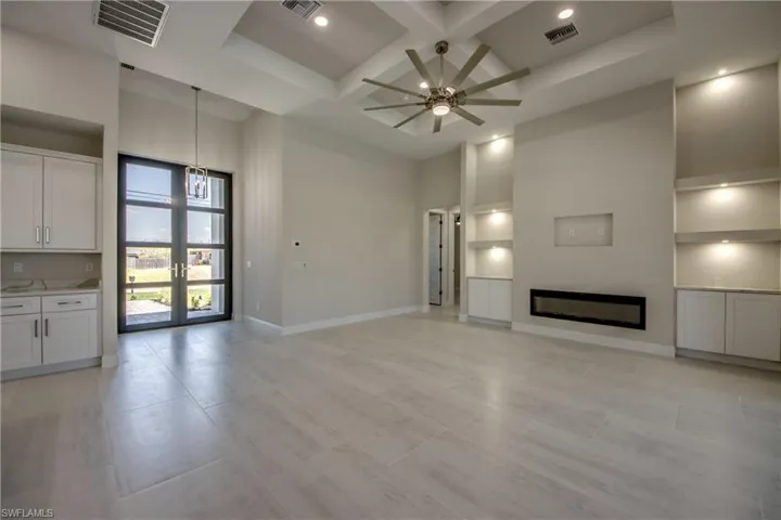 Unfurnished living room featuring visible vents, a high ceiling, coffered ceiling, and baseboards