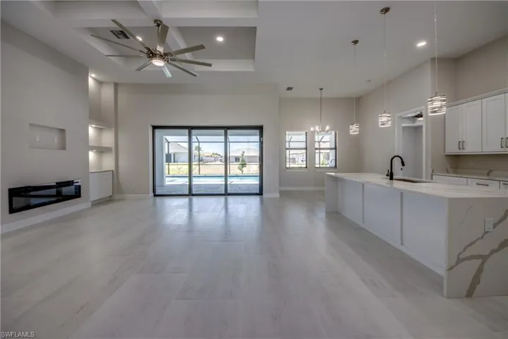 Kitchen with a sink, ceiling fan with notable chandelier, open floor plan, a spacious island, and coffered ceiling