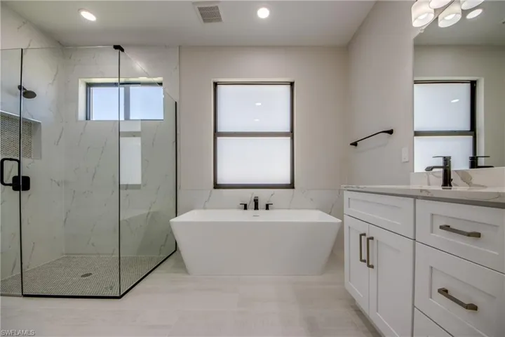 Bathroom featuring visible vents, a freestanding bath, tile walls, vanity, and a marble finish shower