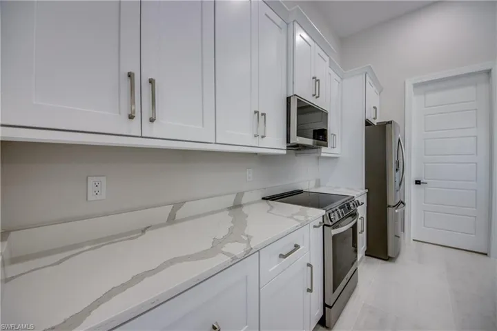 Kitchen with white cabinets, appliances with stainless steel finishes, and light stone counters