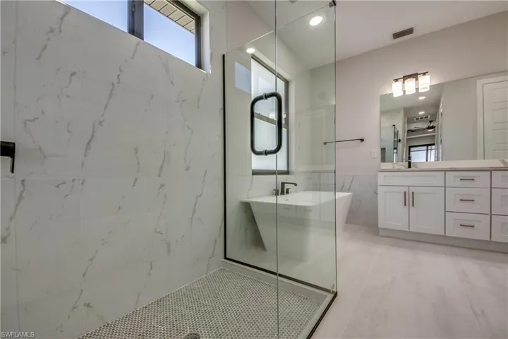 Full bath with visible vents, tile walls, a shower with shower door, vanity, and a soaking tub