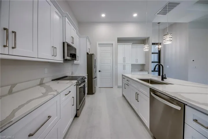 Kitchen with visible vents, white cabinetry, a sink, decorative light fixtures, and stainless steel appliances