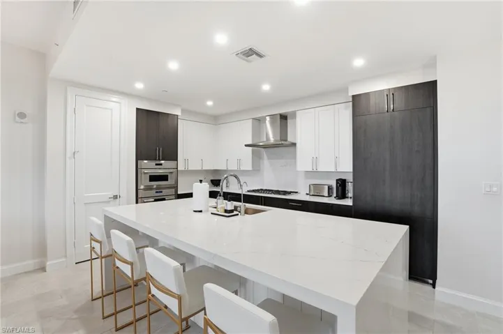 Kitchen featuring white cabinets, a kitchen bar, light stone countertops, a kitchen island with sink, and recessed lighting