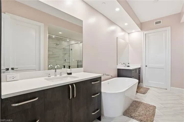 Bathroom with a stall shower, two vanities, a freestanding bath, and recessed lighting