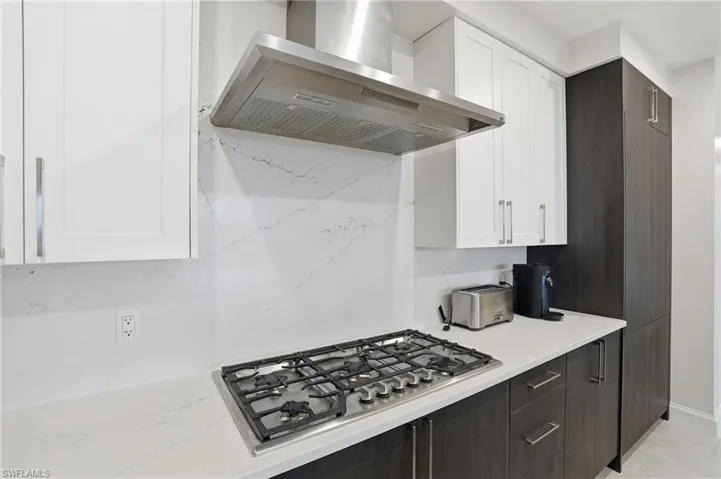 Kitchen featuring white cabinets, wall chimney exhaust hood, dark brown cabinetry, stainless steel gas stovetop, and light stone countertops