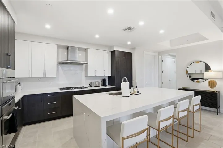 Kitchen with white cabinetry, an island with sink, light stone countertops, a kitchen breakfast bar, and stainless steel appliances