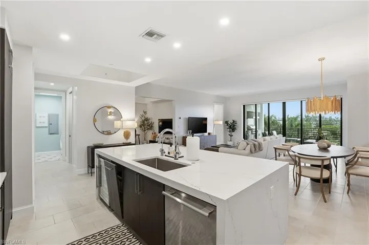 Kitchen with light stone counters, recessed lighting, dishwasher, a chandelier, and a center island with sink