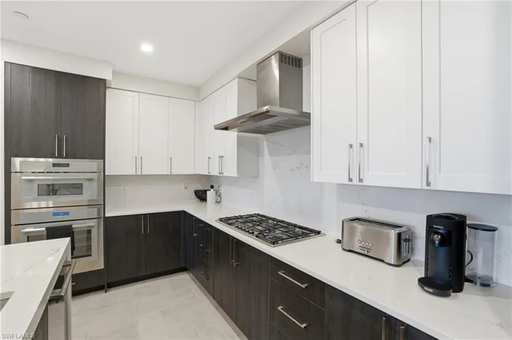 Kitchen featuring white cabinetry, light stone counters, wall chimney exhaust hood, and decorative backsplash