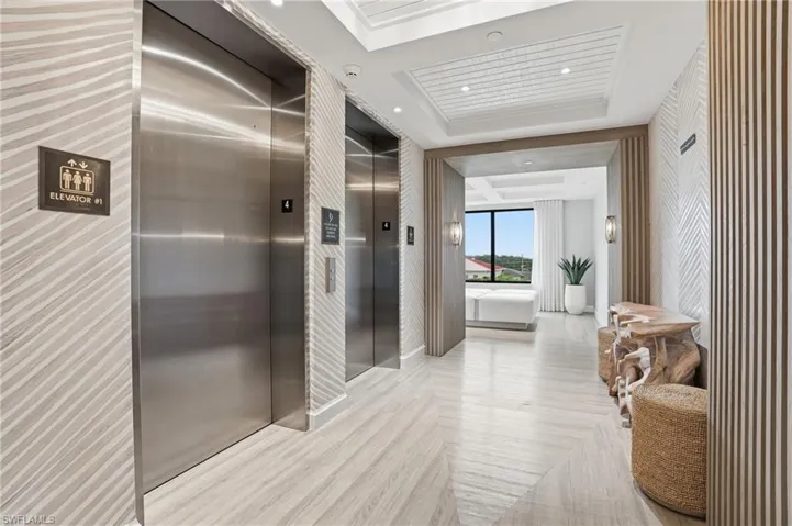 Hallway with a tray ceiling, elevator, and recessed lighting