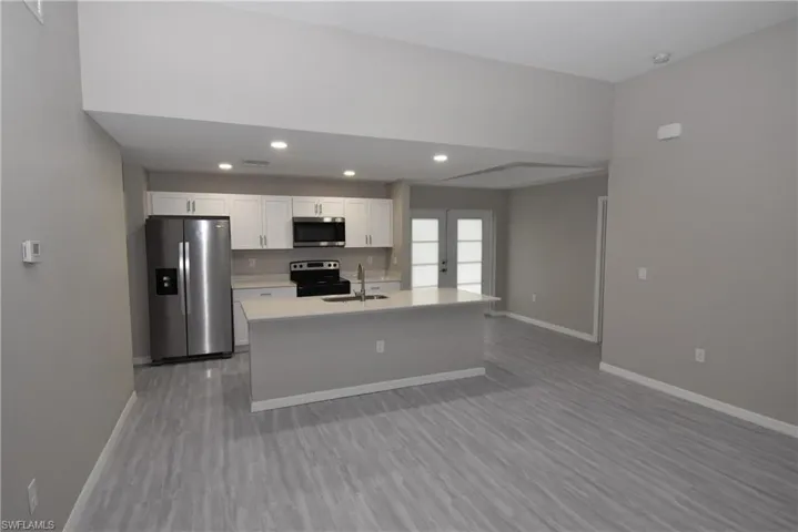 Kitchen with stainless steel appliances, recessed lighting, an island with sink, white cabinets, and french doors