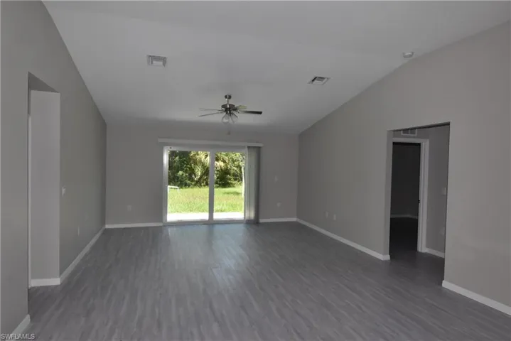 Empty room featuring vaulted ceiling, dark wood-style flooring, and a ceiling fan