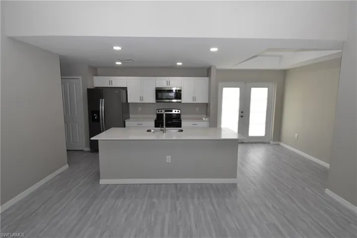 Kitchen with recessed lighting, white cabinets, appliances with stainless steel finishes, a kitchen island with sink, and light wood-style flooring